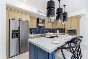 Uma cozinha moderna com uma ilha central, eletrodomésticos de aço inoxidável e luminárias pendentes pretas.