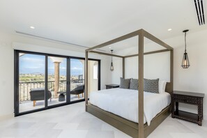 A bedroom with a four-poster bed, a large sliding glass door leading to a balcony, and a view of the landscape.