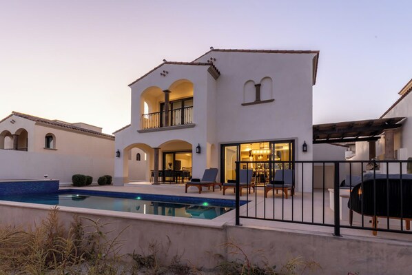 A two-story house with a swimming pool, outdoor seating, and a pergola.