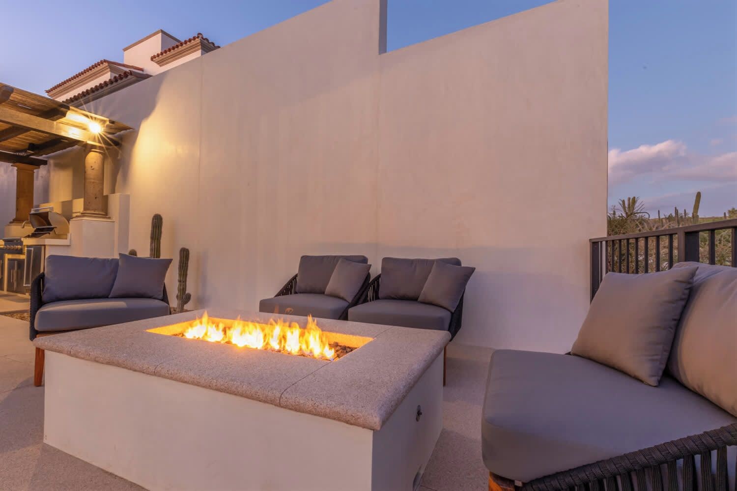 Un área de estar moderna al aire libre con una chimenea, sofás acolchados y una pérgola.
