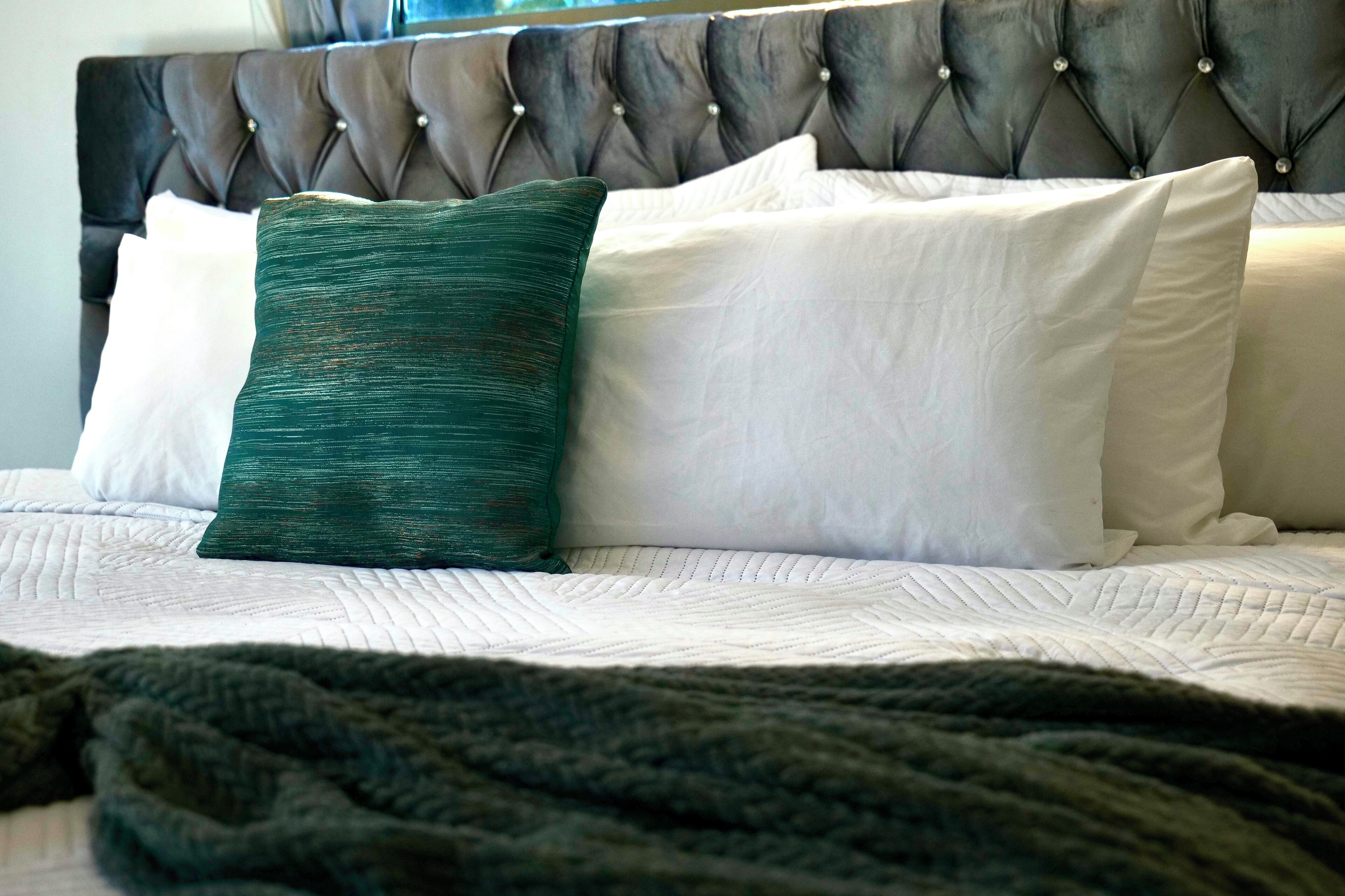 A bed with a tufted headboard, white and green pillows, and a dark green blanket.