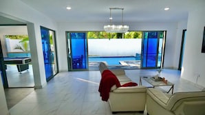 Un moderno salón con vista a la piscina, una araña y un plaid rojo sobre el sofá.