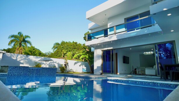 Una casa moderna de dos pisos con piscina, ventanas amplias y un balcón.