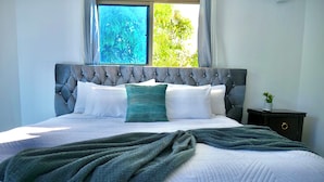 Una cama bien tendida con un cabecero acolchado, ropa de cama blanca y una manta verde.