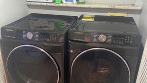 Deux lave-linge Samsung noirs à chargement frontal, installés dans une buanderie dont le sol est en bois.