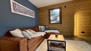 A modern living room with a brown leather sofa, a small wooden coffee table, and a large window with a view of a snowy landscape. - Cozy T2 and mountain area, a stone's throw from the slopes! (CHATEL)