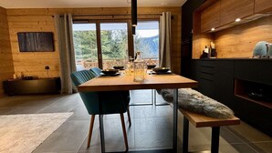 A modern dining area with a wooden table, chairs, and a bench. There is a view of mountains through large windows. - Cozy T2 and mountain area, a stone's throw from the slopes! (CHATEL)