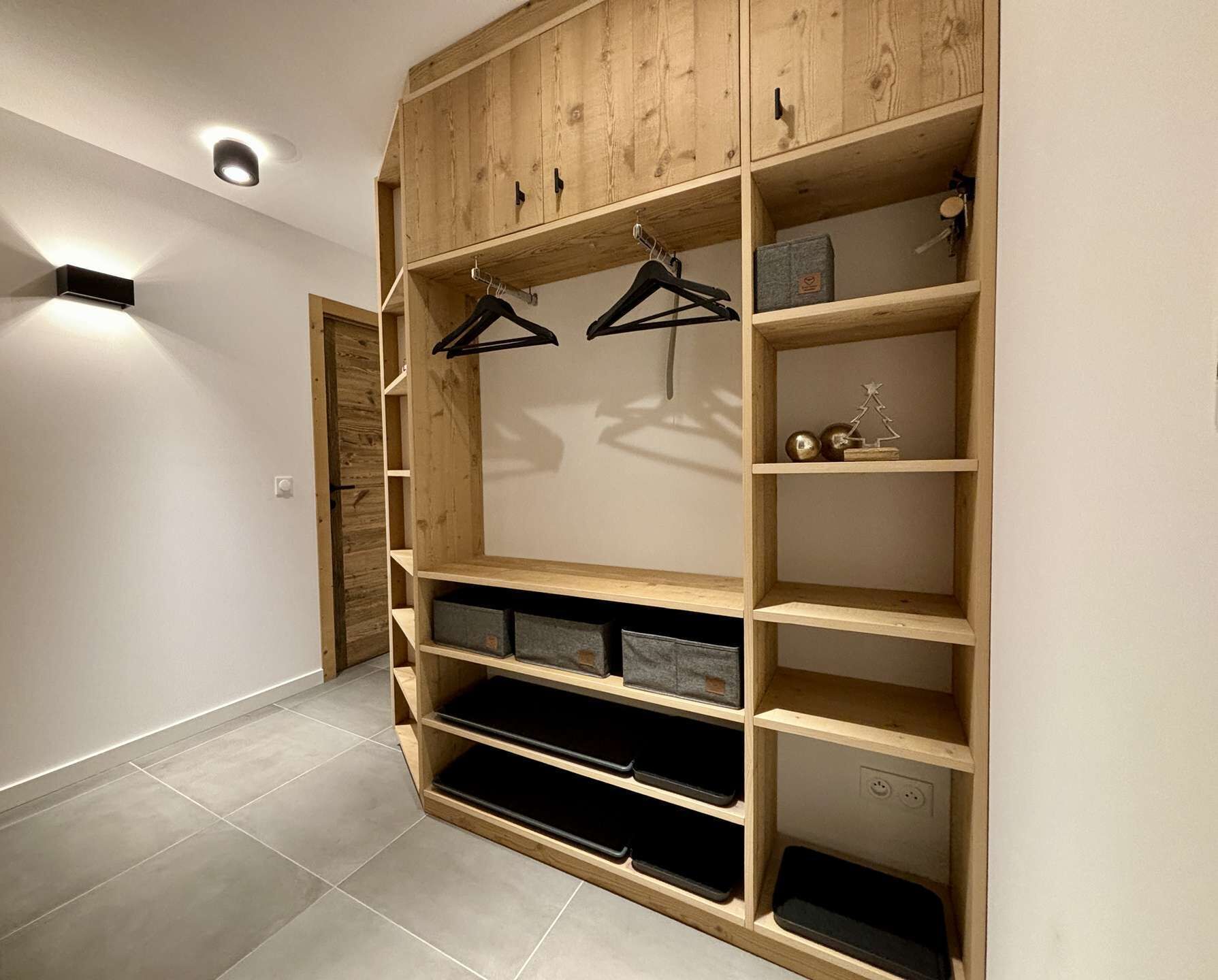 Un armario de madera con varios estantes y espacio para colgar, un pequeño estante con objetos decorativos, y un piso de baldosas.