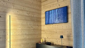 A modern room with wooden panel walls, a large framed artwork, a black console table, and a floor lamp. - Cozy T2 and mountain area, a stone's throw from the slopes! (CHATEL)