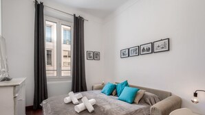 Une chambre à coucher avec un lit, un bureau, une chaise et une fenêtre avec des rideaux. Il y a des tableaux accrochés au mur.