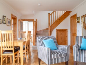 A spacious living area with a wooden dining table and chairs, a striped armchair with a blue pillow, and a wooden staircase. - Creagan by Interhome (North Skye)