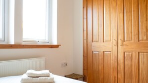 A bedroom with a bed, a wooden wardrobe, a window, and a radiator. - Creagan by Interhome (North Skye)