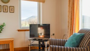 A living room with a television on a stand, a striped sofa, a wooden table, and a window with a view of mountains. - Creagan by Interhome (North Skye)