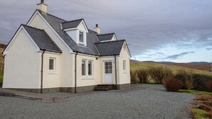 A two-story house with a steeply pitched roof, a chimney, and a gravel driveway leading to a front door. - Creagan by Interhome (North Skye)