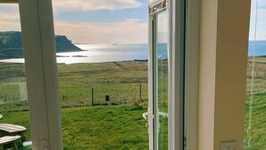 Ein Zimmer mit einer großen Schiebeglastür, die zu einem malerischen Blick auf eine Küstenlandschaft führt, mit Wasser und fernen Hügeln.