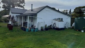 A white house with a porch, surrounded by green grass and potted plants. - Quintessential Tassie Shack (South Mount Cameron)