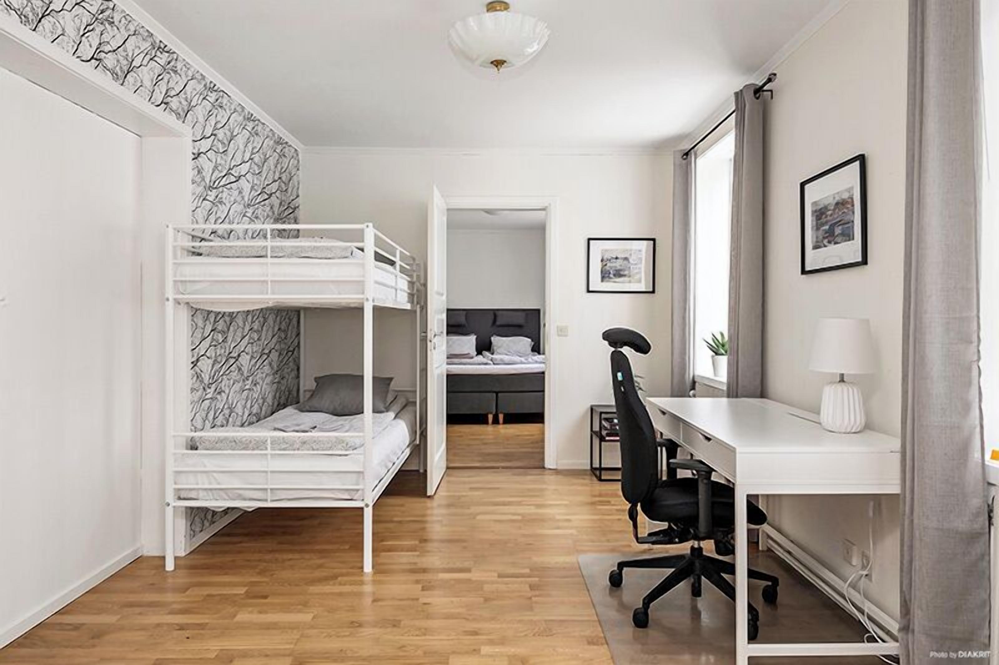 Une chambre avec un lit superposé, un bureau avec une chaise, une lampe et une fenêtre avec des rideaux.