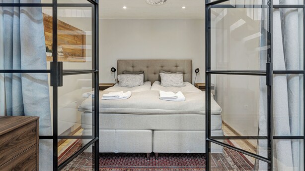 A bedroom with a large bed, a wooden dresser, and a patterned rug. - HernöRum - Storgatan (Harnosand)