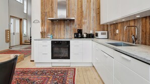 A modern kitchen with a central island, white cabinetry, a stainless steel range hood, and a wooden accent wall. - HernöRum - Storgatan (Harnosand)