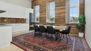 A modern kitchen with white cabinets, a wooden accent wall, and a dining area with a patterned rug and black chairs. - HernöRum - Storgatan (Harnosand)