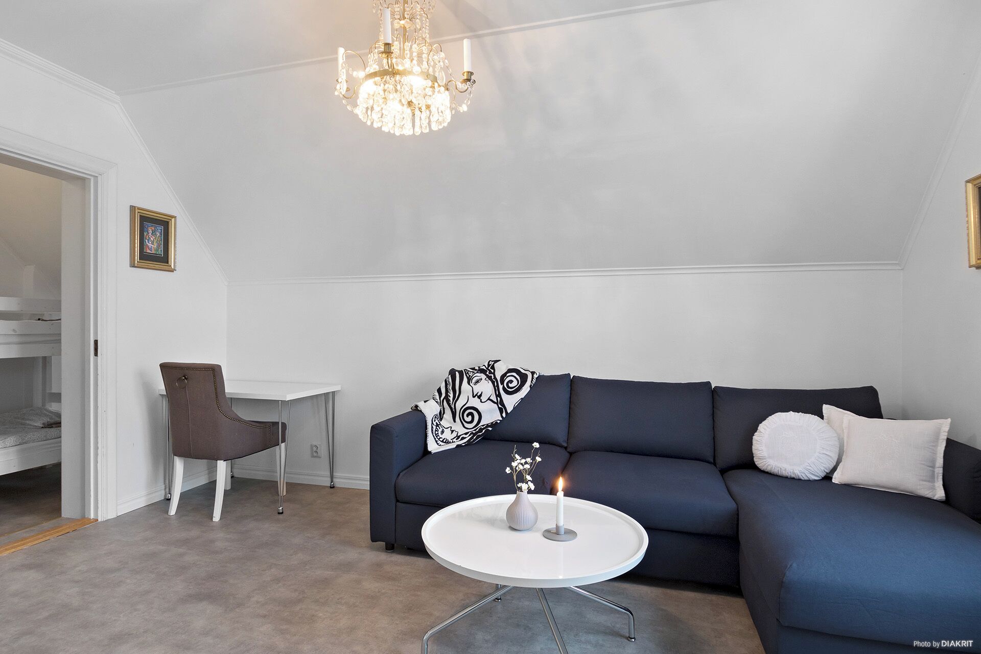 Una sala de estar con un sofá azul oscuro, una mesita blanca con una vela y un sillón marrón.