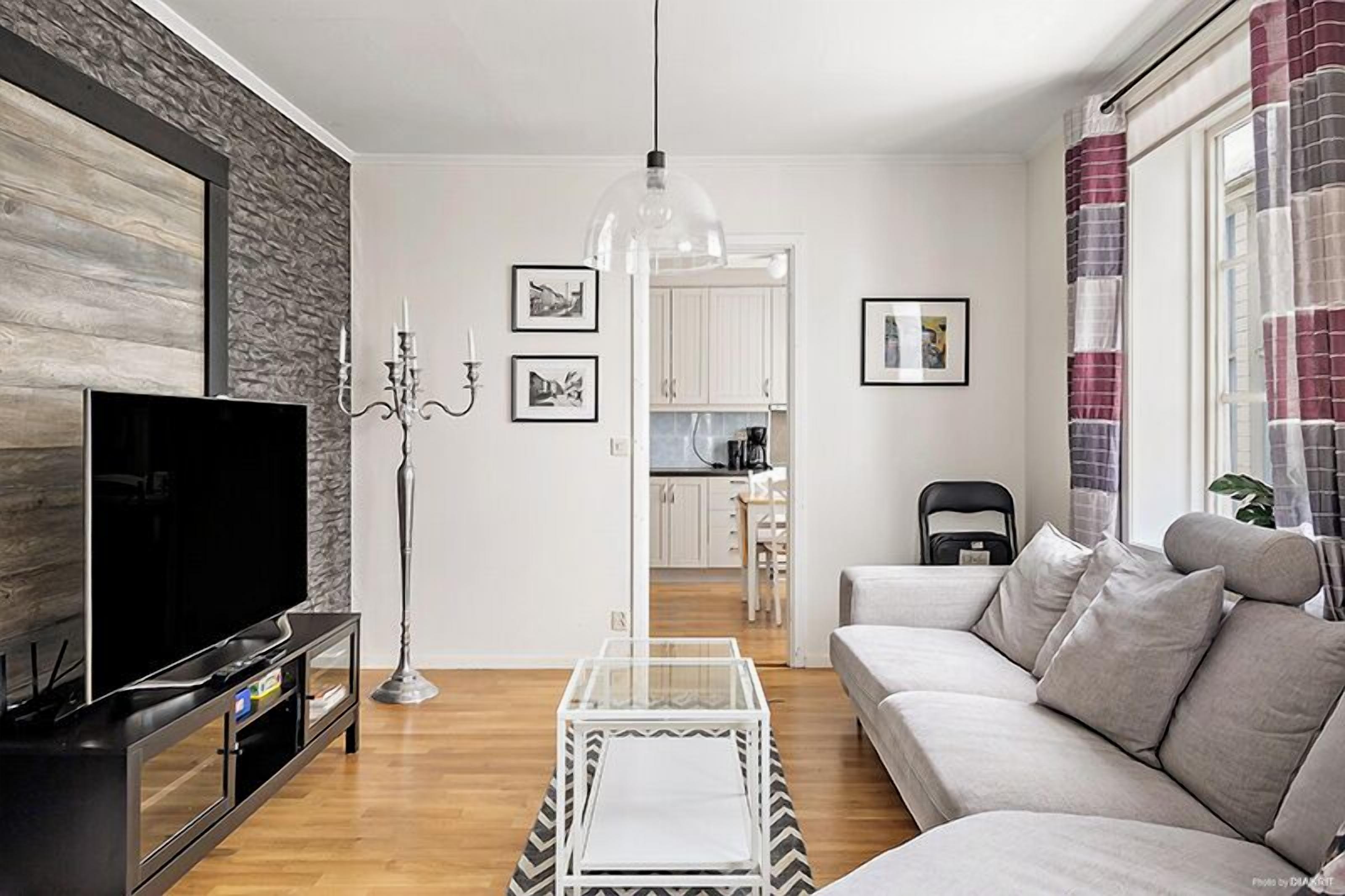 Ett modernt vardagsrum med en platt-TV, ett soffbord i glas, en soffa och en matplats i bakgrunden.