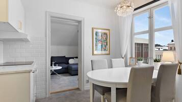 A modern kitchen with white cabinetry, a round dining table with chairs, a chandelier, and a painting on the wall.