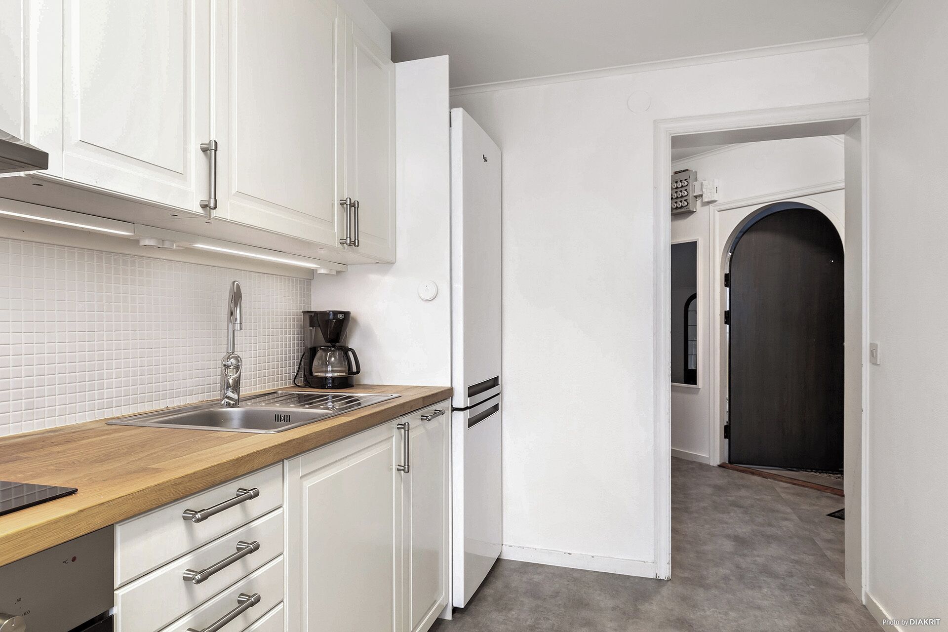 A kitchen with white cabinets, a wooden countertop, a coffee maker, and a refrigerator.
