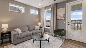 A living room with a grey sofa, two side tables with lamps, a round coffee table, and a view of a dock with boats.
