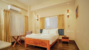 A bedroom with a wooden bed, a small bedside table, a chair, a table, and an air conditioning unit. - Hotel Khamsum (Phuntsholing)