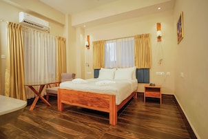 A bedroom with a wooden bed, a small bedside table, a chair, a table, and an air conditioning unit.