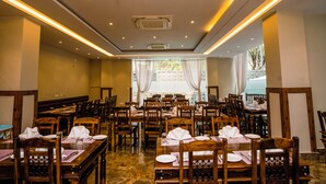 A restaurant with wooden tables and chairs, arranged in a spacious layout with a view of the outdoors. - Hotel Khamsum (Phuntsholing)