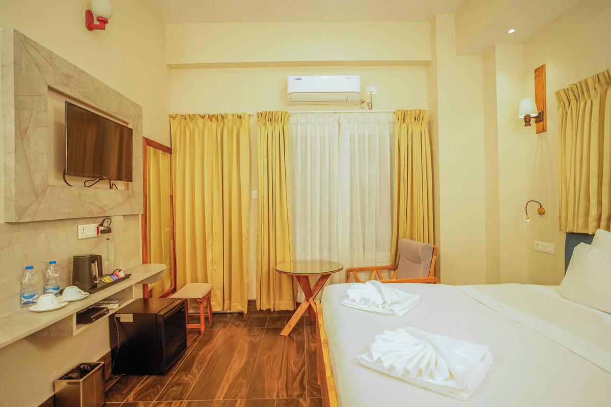Quarto de hotel com cama, escrivaninha com televisão, mesinha e uma cadeira.