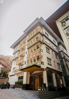 Un edificio de varios pisos con balcones, una entrada central y un letrero que dice "Khamsum".