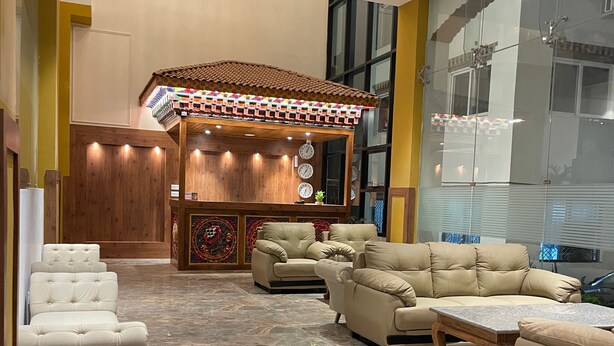 A spacious lobby with a central seating area featuring sofas and a coffee table, a decorative wall with clocks, and a large window providing a view of the outside. - Hotel Khamsum (Phuntsholing)