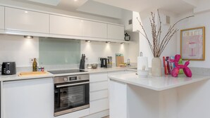 Une cuisine moderne avec des meubles blancs, un four encastré et un plan de travail sur lequel se trouvent divers appareils et ustensiles.