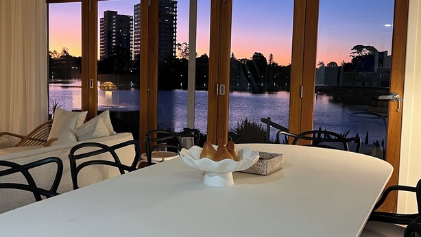 A dining area with a table and chairs, a decorative centerpiece, and a view of a body of water and buildings at dusk.