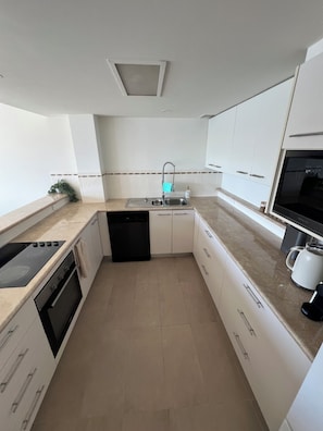 A modern kitchen with white cabinets, a black dishwasher, a stove, and a coffee maker. - The Master Suite (Mermaid Waters)