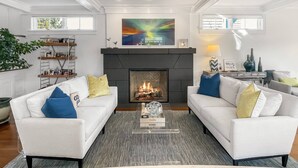 Een woonkamer met twee witte banken, een open haard, en een groot abstract schilderij erboven.