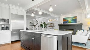 Een moderne keuken met een centraal eiland, roestvrijstalen apparatuur en hangende verlichting.