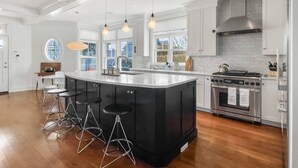 Een moderne keuken met een groot eiland, barstoelen, roestvrijstalen apparatuur en grote ramen.