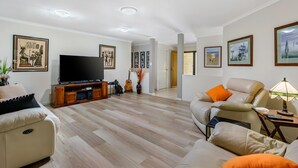 Una sala de estar amplia con televisor de pantalla plana, sofás de cuero, piso de madera y obras de arte en las paredes.