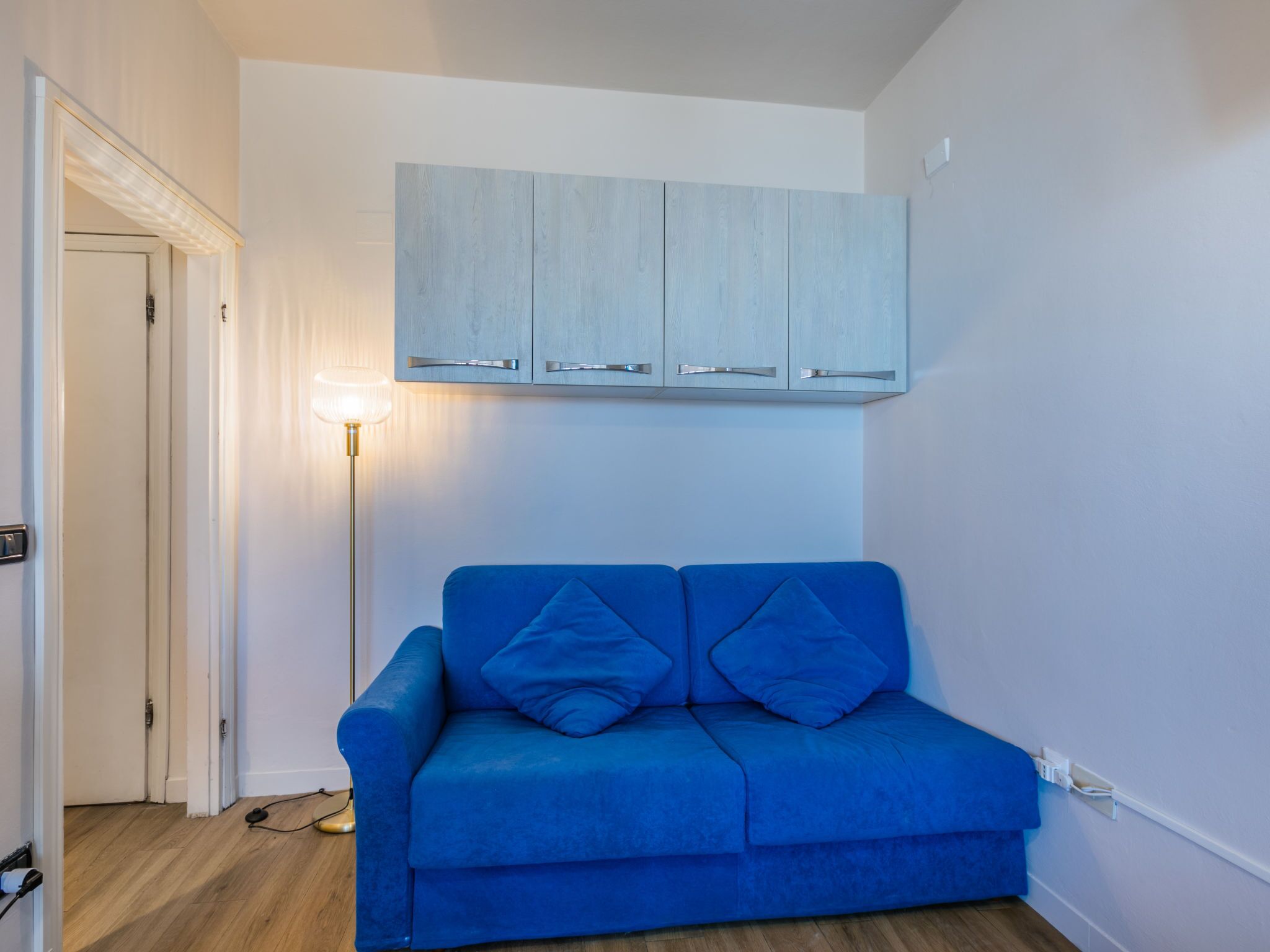 A room with a blue sofa, a floor lamp, and a light blue cabinet.
