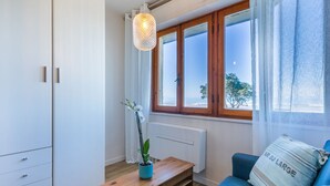 Una habitación con un banco de madera, un sofá azul, un armario blanco y una ventana con vista al mar.