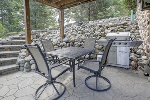 Eine Terrasse im Freien mit Grill, Steintreppe und Metallstühlen.