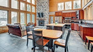 A spacious log cabin interior with a stone fireplace, wooden dining table, and large windows. - Lakefront Gem w/ Dock & Views in Lac Du Flambeau (Lac Du Flambeau)