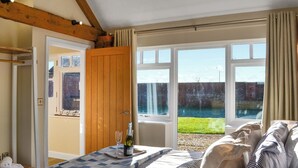 Un dormitorio con una cama grande, una ventana que ofrece vista a un muro de ladrillo y vegetación, y una puerta de madera.