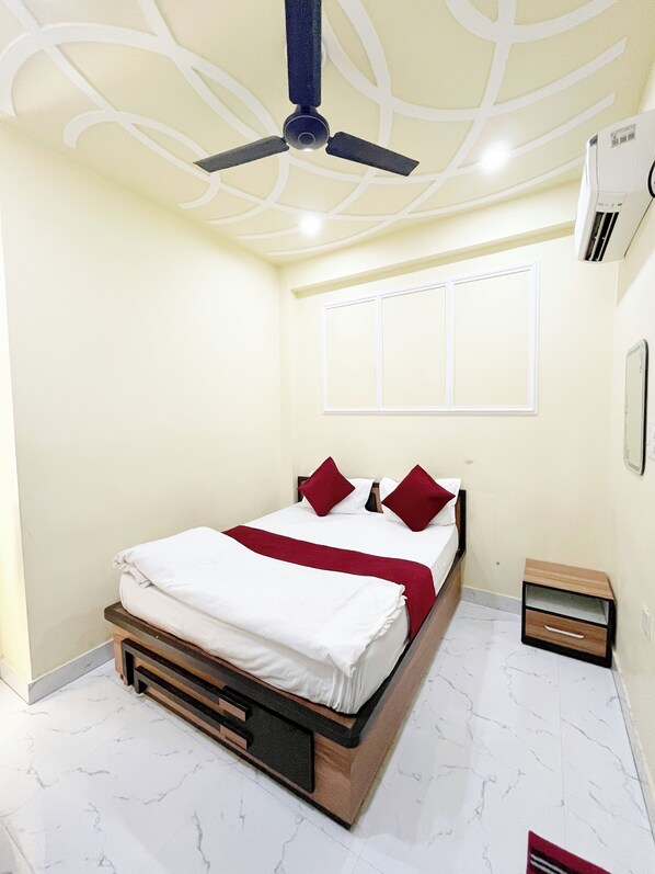 A neatly arranged bedroom with a bed, a ceiling fan, an air conditioning unit, and a bedside table.