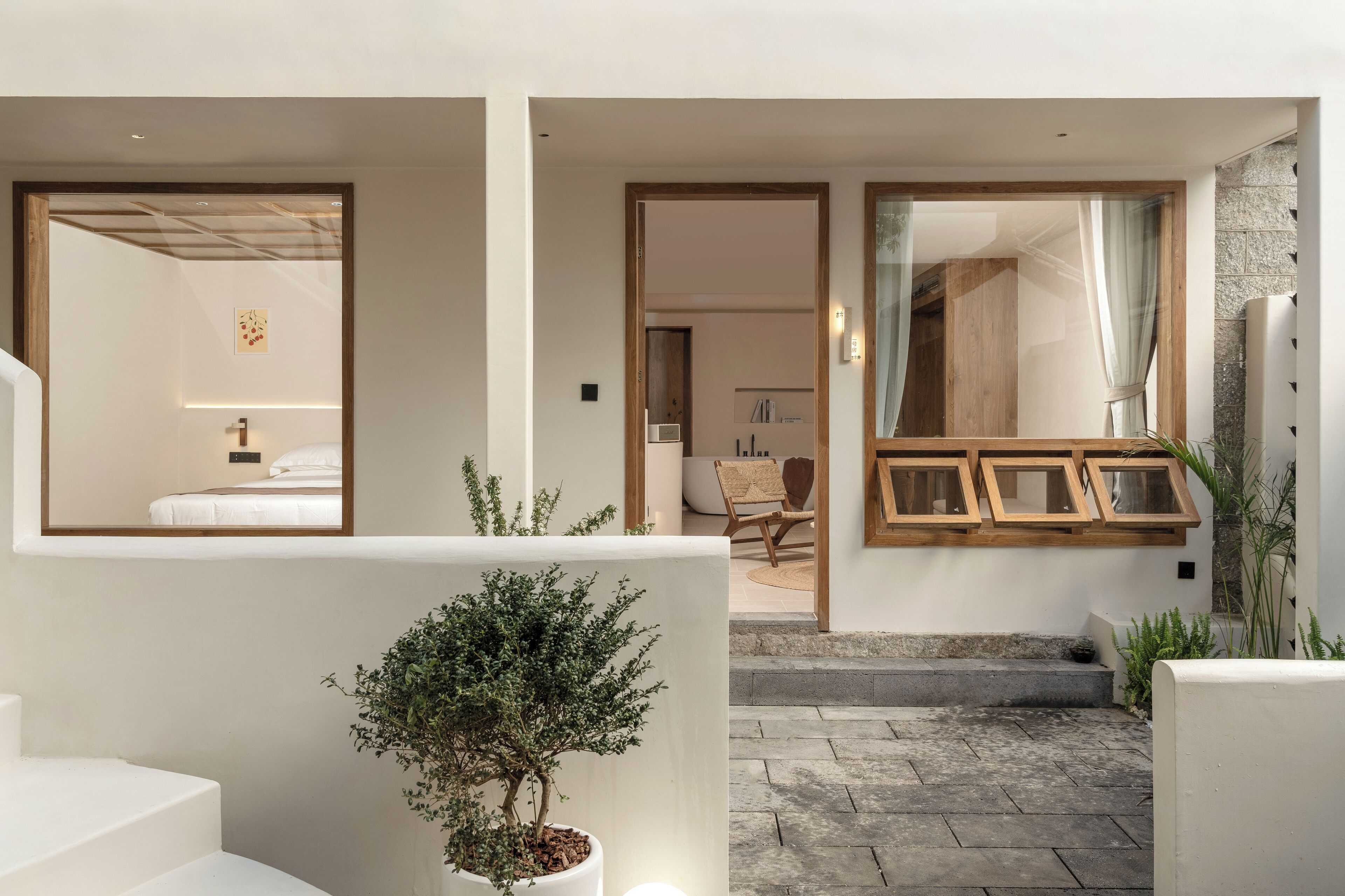 Interior de un hotel moderno con un diseño limpio y minimalista, que incluye una escalera, una pequeña planta en maceta y vistas a la habitación contigua.