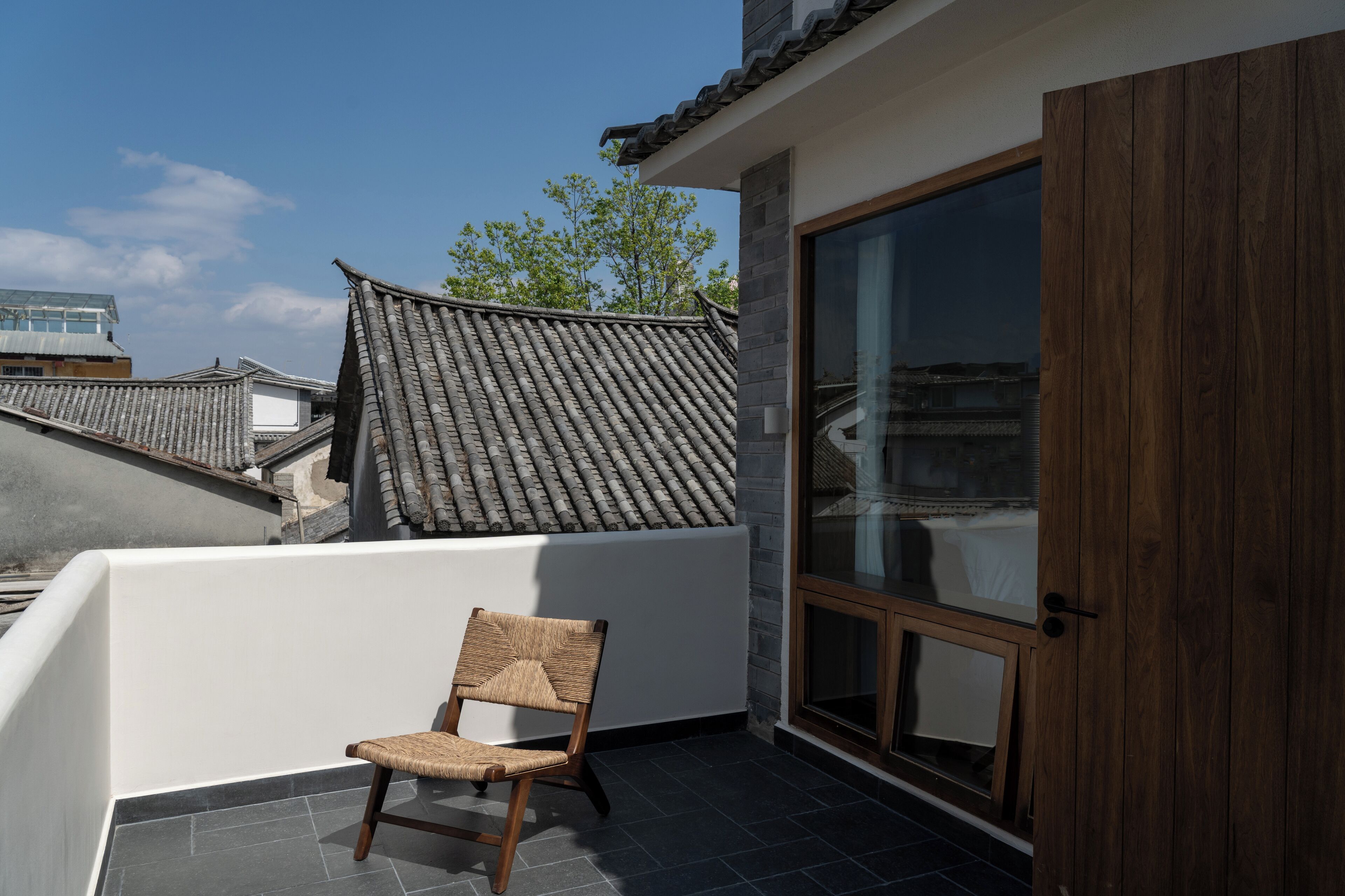 Un balcon avec une chaise, un toit traditionnel recouvert de tuiles et une porte-fenêtre coulissante.